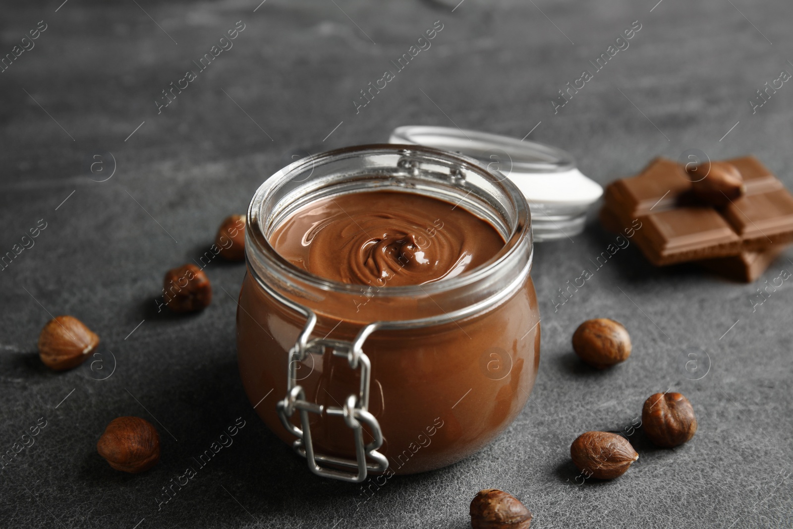 Photo of Composition with tasty chocolate cream in glass jar and hazelnuts on table