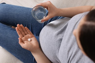 Photo of Pregnant woman with glass of water and pill at home, above view