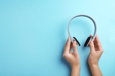 Photo of Woman holding headphones on color background, top view. Space for text