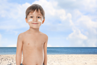 Adorable little boy with sun protection cream on face at sandy beach, space for text 