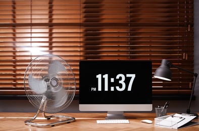 Photo of Modern electric fan and computer on table in office