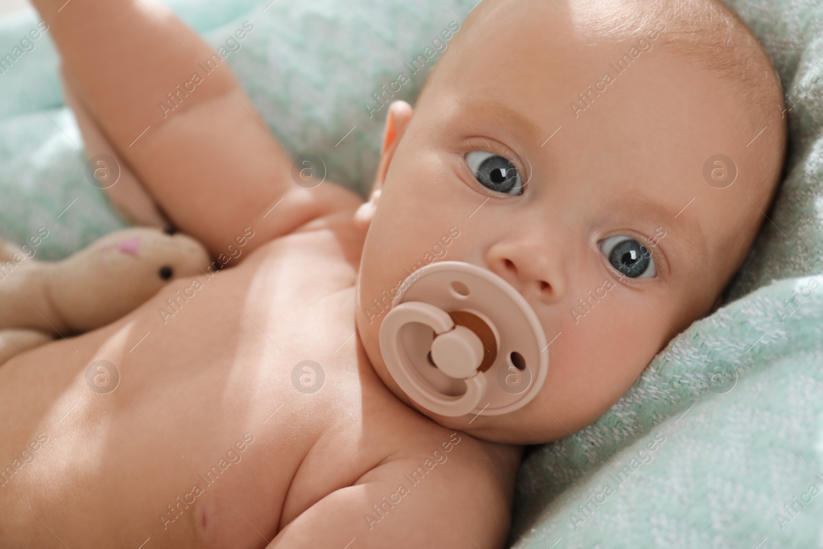 Photo of Cute little baby with pacifier lying on soft blanket, closeup