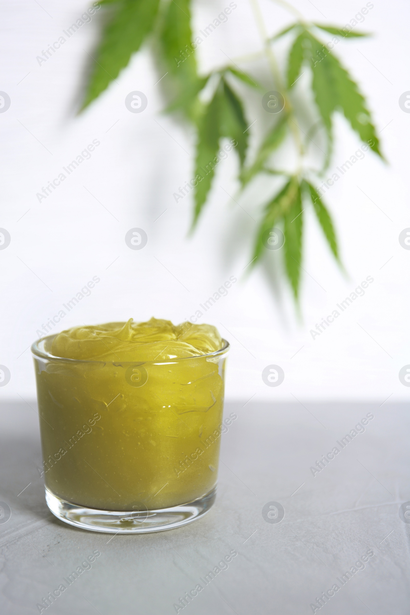 Photo of Glass with organic hemp lotion on table against light background