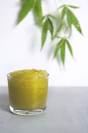 Photo of Glass with organic hemp lotion on table against light background