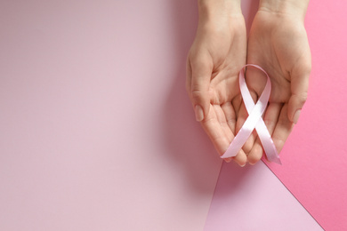 Woman holding pink ribbon on color background, top view with space for text. Breast cancer awareness