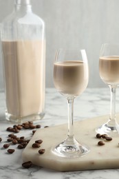 Coffee cream liqueur in glasses, beans and bottle on white marble table