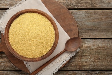 Photo of Bowl of raw couscous and spoon on wooden table, top view. Space for text