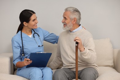 Health care and support. Nurse holding clipboard and laughing with elderly patient on sofa indoors