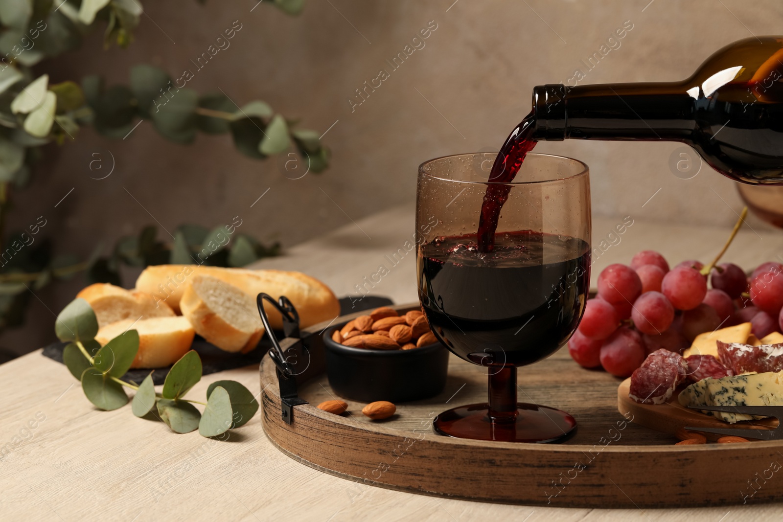 Photo of Pouring red wine into glass at wooden table, closeup