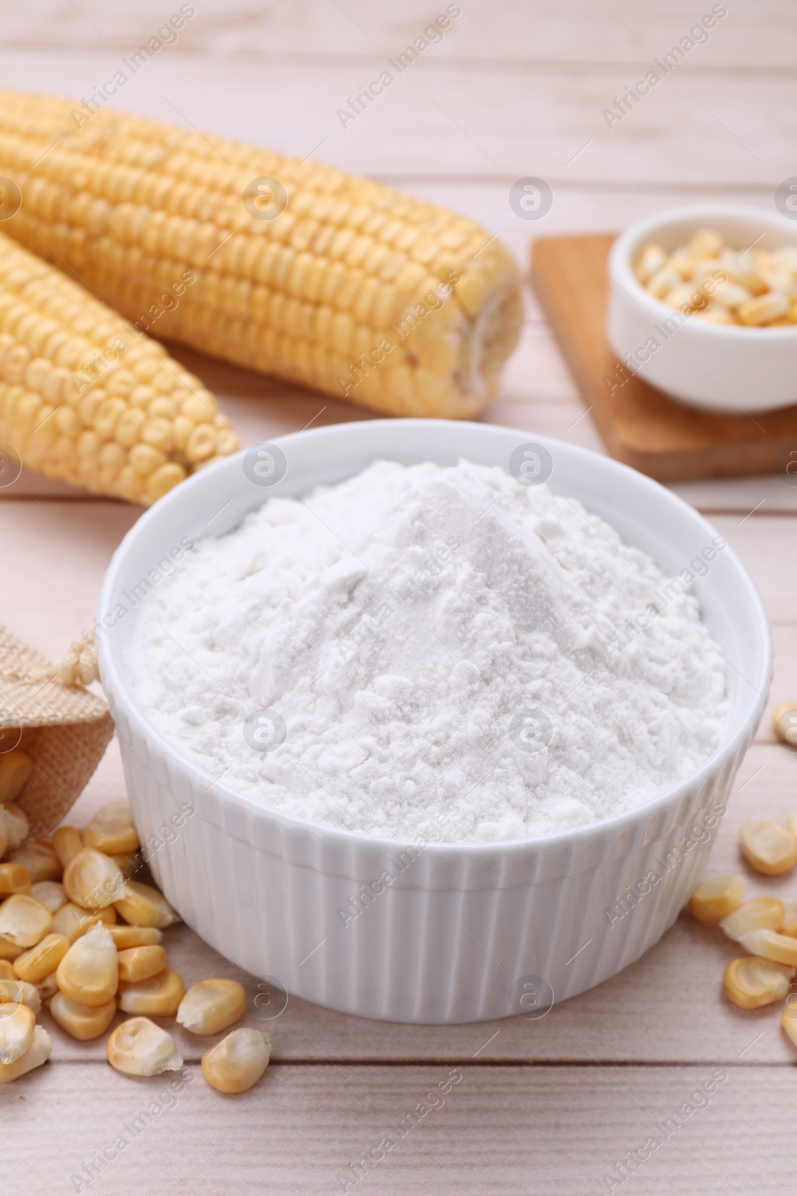 Photo of Bowl with corn starch, ripe cobs and kernels on wooden table