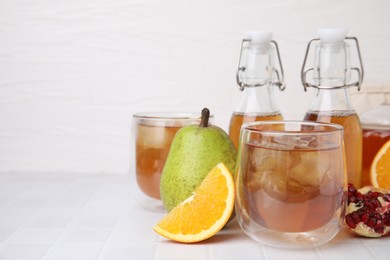 Tasty kombucha with ice cubes and fresh fruits on white tiled table, space for text