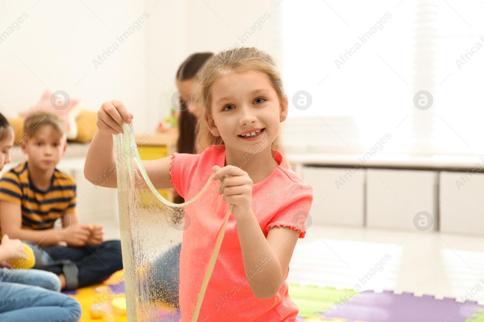 Photo of Happy little girl playing with slime in room