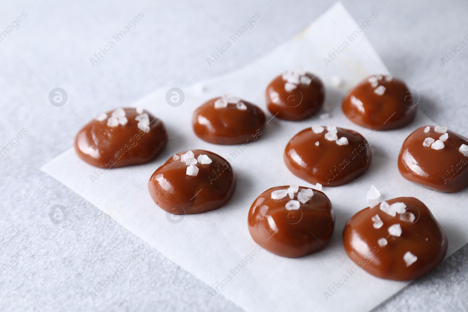 Photo of Tasty caramel candies and salt on light grey table, closeup