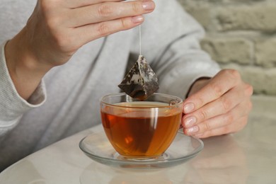 Photo of Woman taking tea bag out of cup at table indoors, closeup