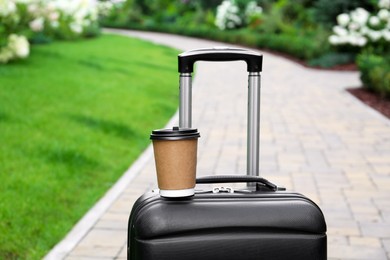 Paper cup of hot coffee on suitcase outdoors. Takeaway drink