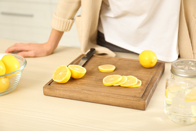 Photo of Young woman making lemon water in kitchen, closeup