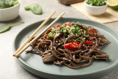 Photo of Tasty buckwheat noodles (soba) with chili pepper, onion and chopsticks on light table, closeup