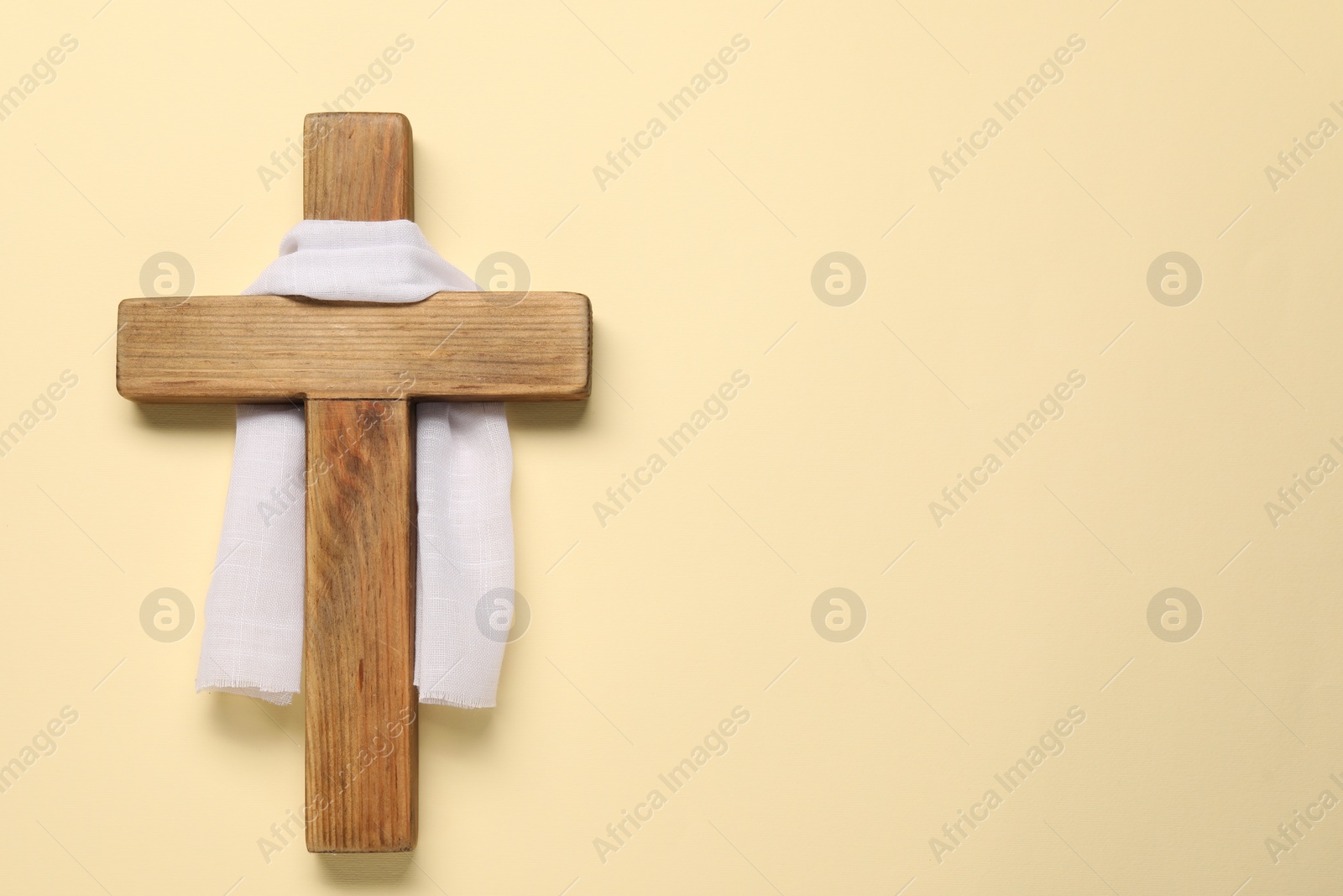 Photo of Wooden cross and white cloth on beige background, top view with space for text. Easter attributes