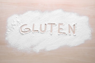Photo of Word Gluten written with flour on wooden table, top view