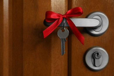 Photo of House key with red bow on door handle, closeup. Housewarming party