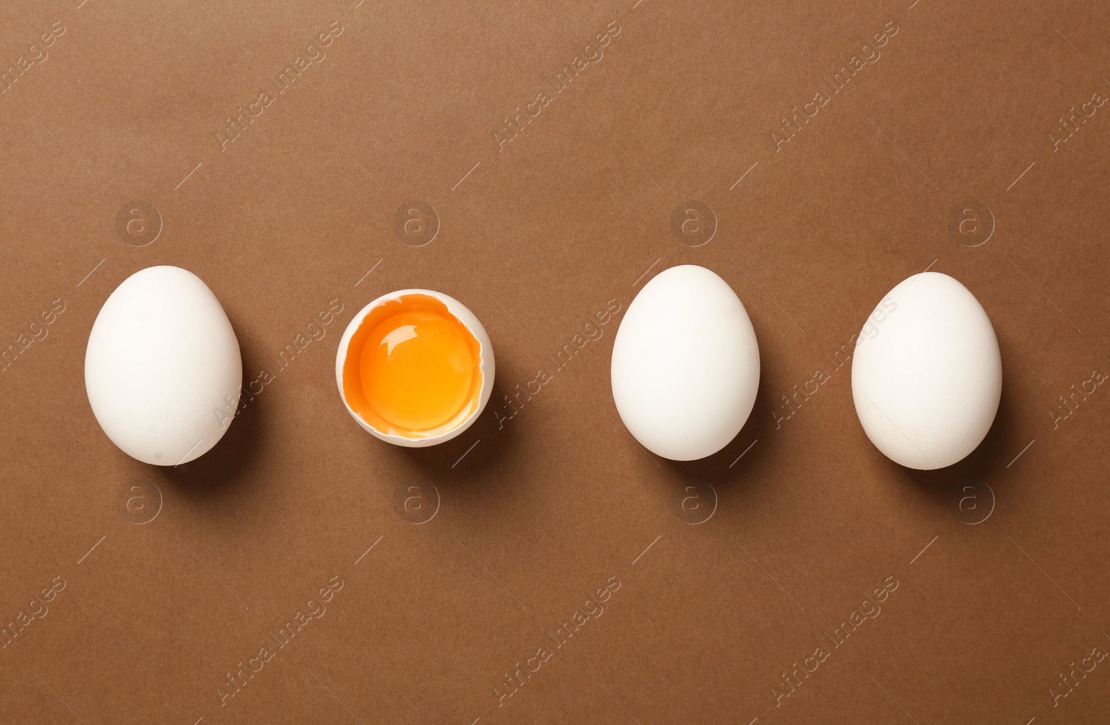 Photo of Whole and broken chicken eggs on brown background, flat lay