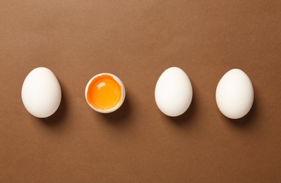 Whole and broken chicken eggs on brown background, flat lay