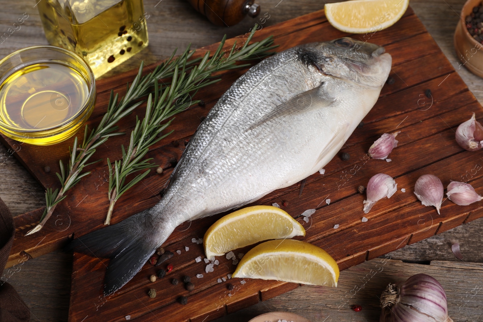 Photo of Raw dorado fish, lemon wedges, spices and oil on wooden table