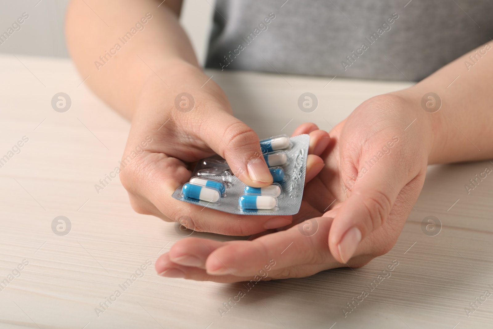 Photo of Woman holding blister of pills at white wooden table, closeup