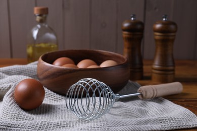 Photo of Making dough. Metal whisk and eggs in wooden bowl on table, closeup