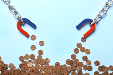 Chain with magnets attracting coins on light blue background, flat lay