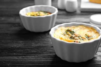 Photo of Tasty broccoli casserole in ramekins on black wooden table