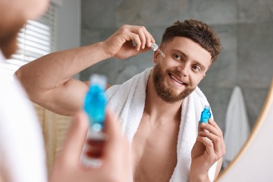 Photo of Handsome man applying serum onto his face near mirror in bathroom