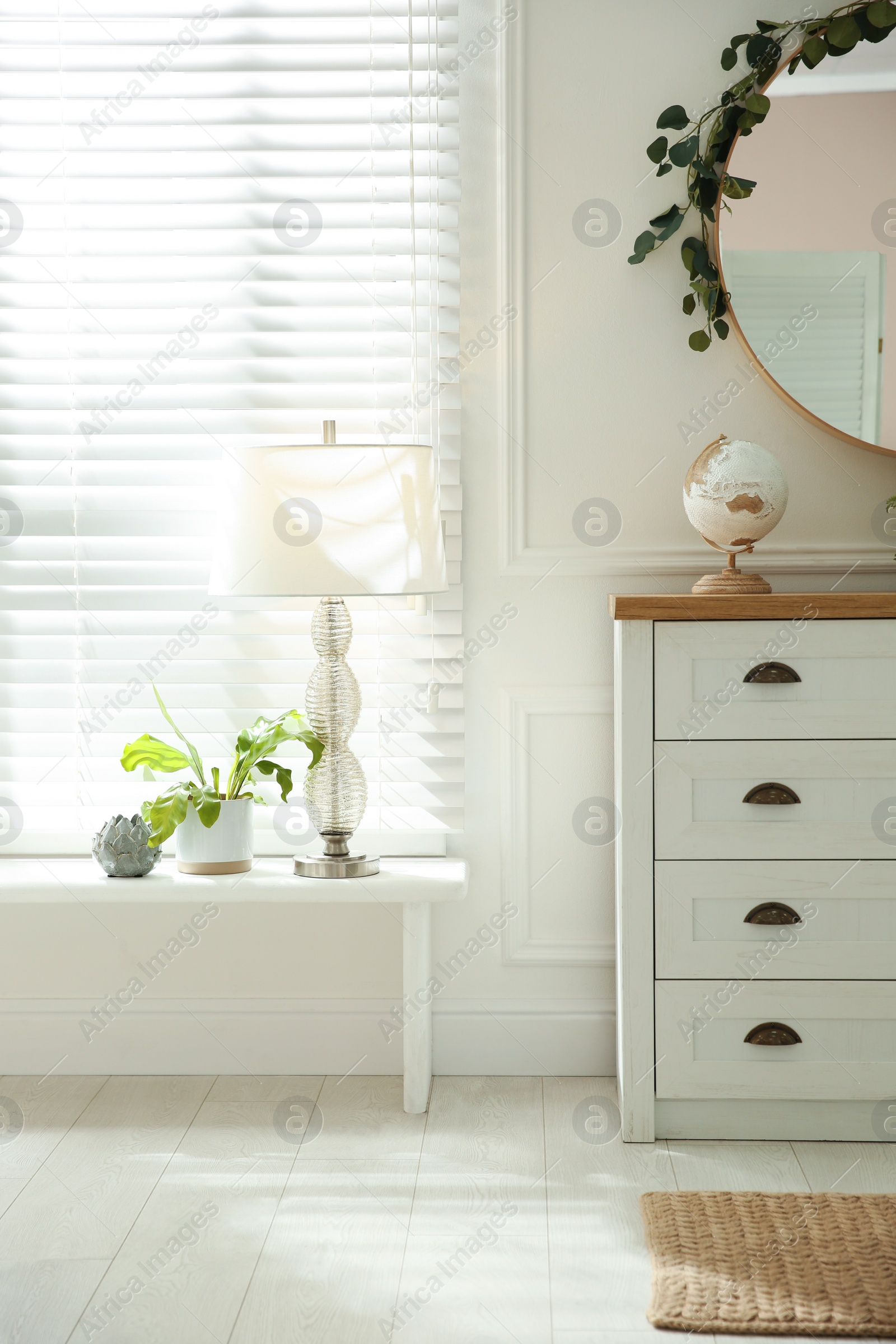 Photo of White chest of drawers and mirror near window indoors. Interior design