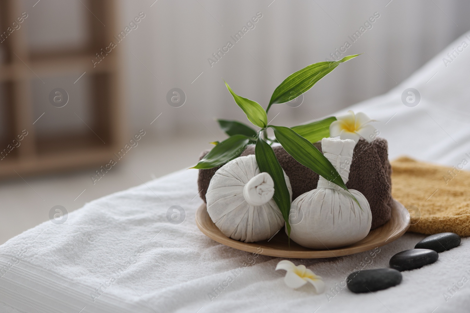 Photo of Spa stones, flowers, towel and herbal bags on massage table indoors