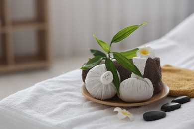 Photo of Spa stones, flowers, towel and herbal bags on massage table indoors