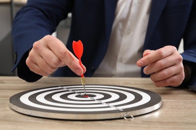 Photo of Business targeting concept. Man with dart aiming at dartboard at wooden table indoors, closeup