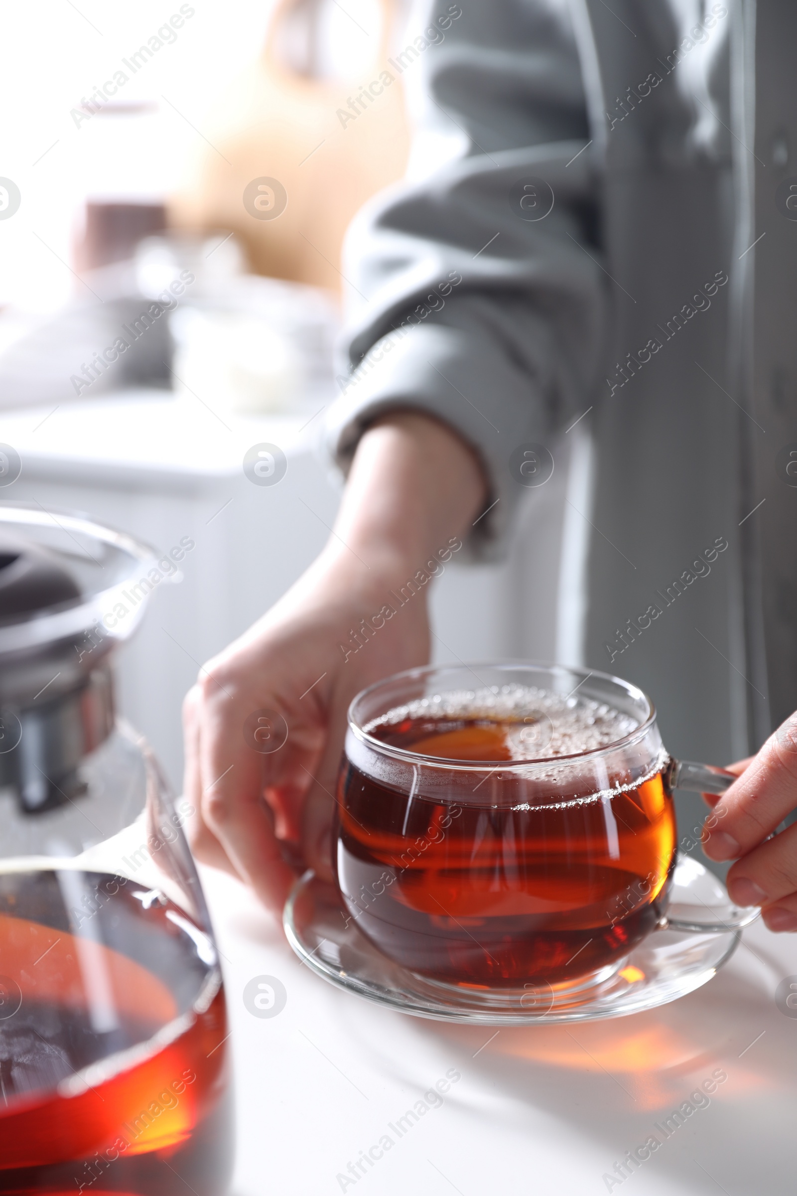 Photo of Woman with cup of hot tea at white table, closeup