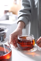 Photo of Woman with cup of hot tea at white table, closeup