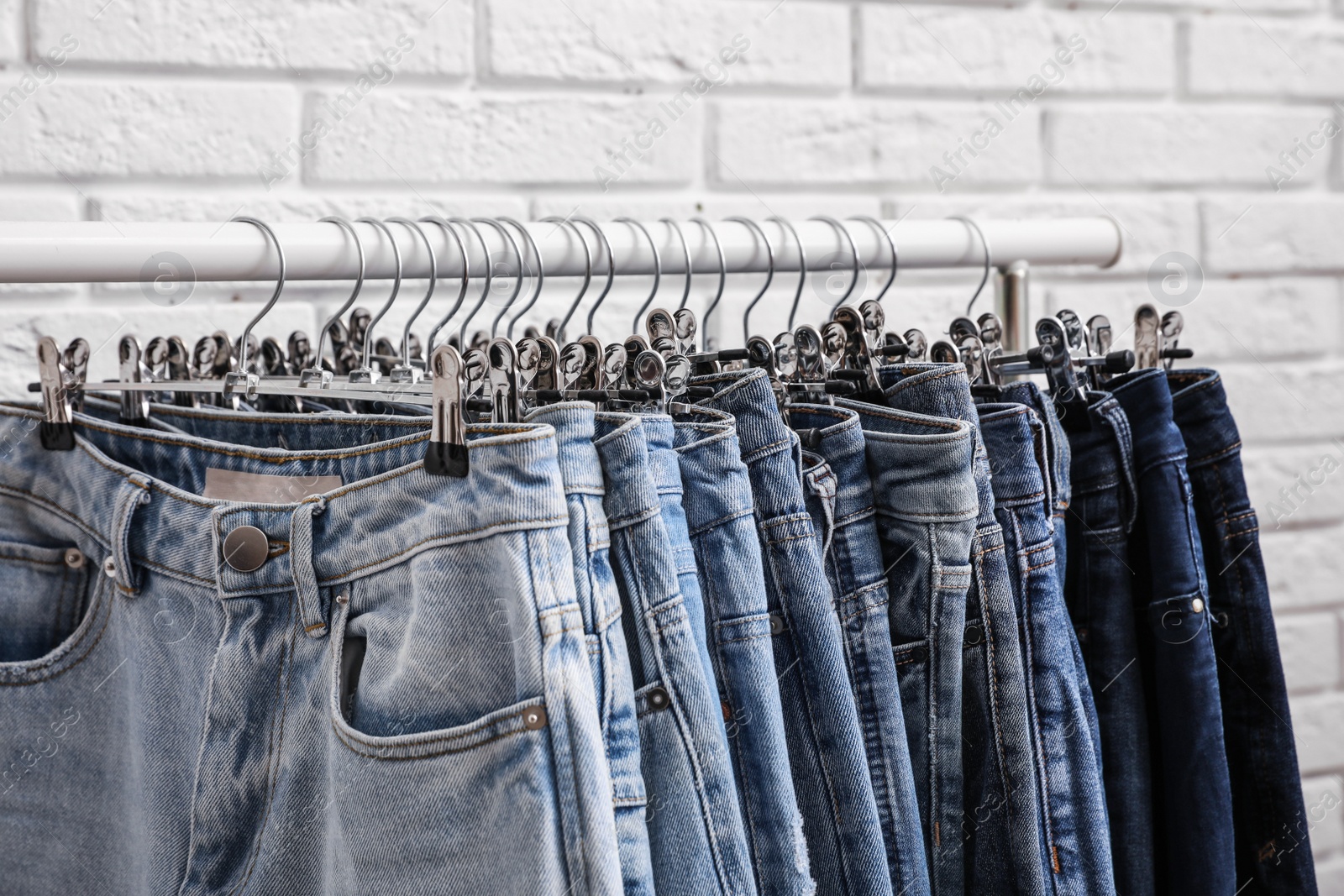 Photo of Rack with stylish jeans near brick wall, closeup