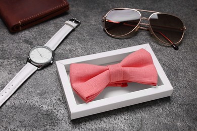Photo of Stylish coral bow tie, sunglasses and wristwatch on grey textured background