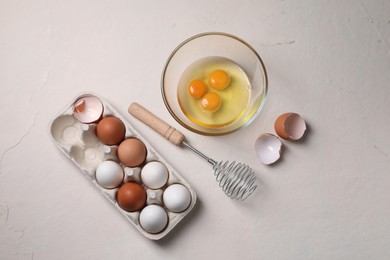 Photo of Metal whisk, raw eggs and shells on light table, flat lay