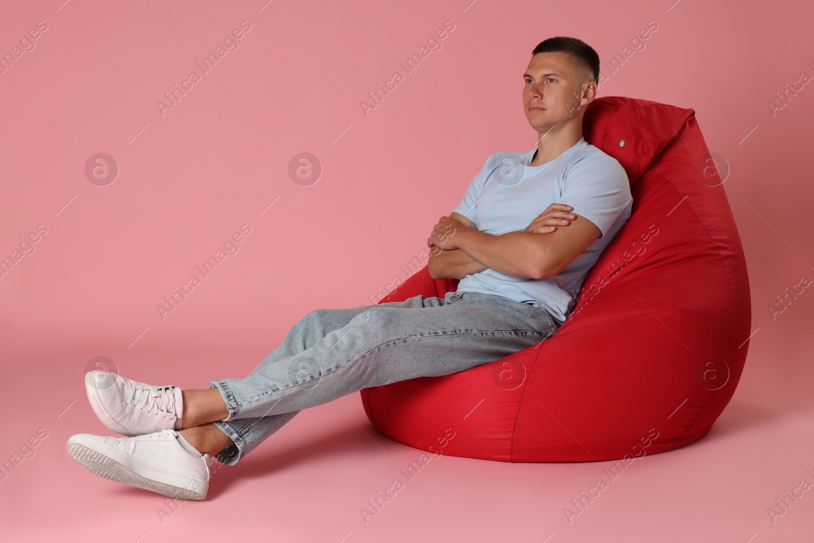 Photo of Handsome man on red bean bag chair against pink background