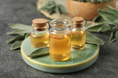 Photo of Bottles of essential sage oil and leaves on grey table