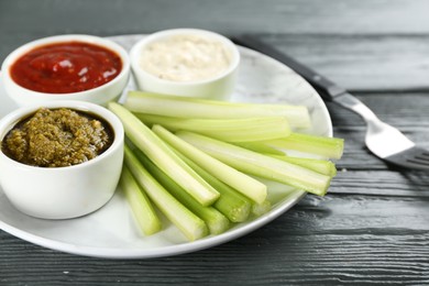 Plate with celery sticks and different dip sauces on grey wooden table, closeup