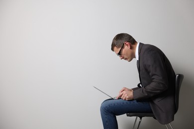 Man with bad posture using laptop while sitting on chair against grey background. Space for text