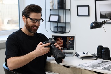 Photo of Professional photographer in glasses holding digital camera at table in office