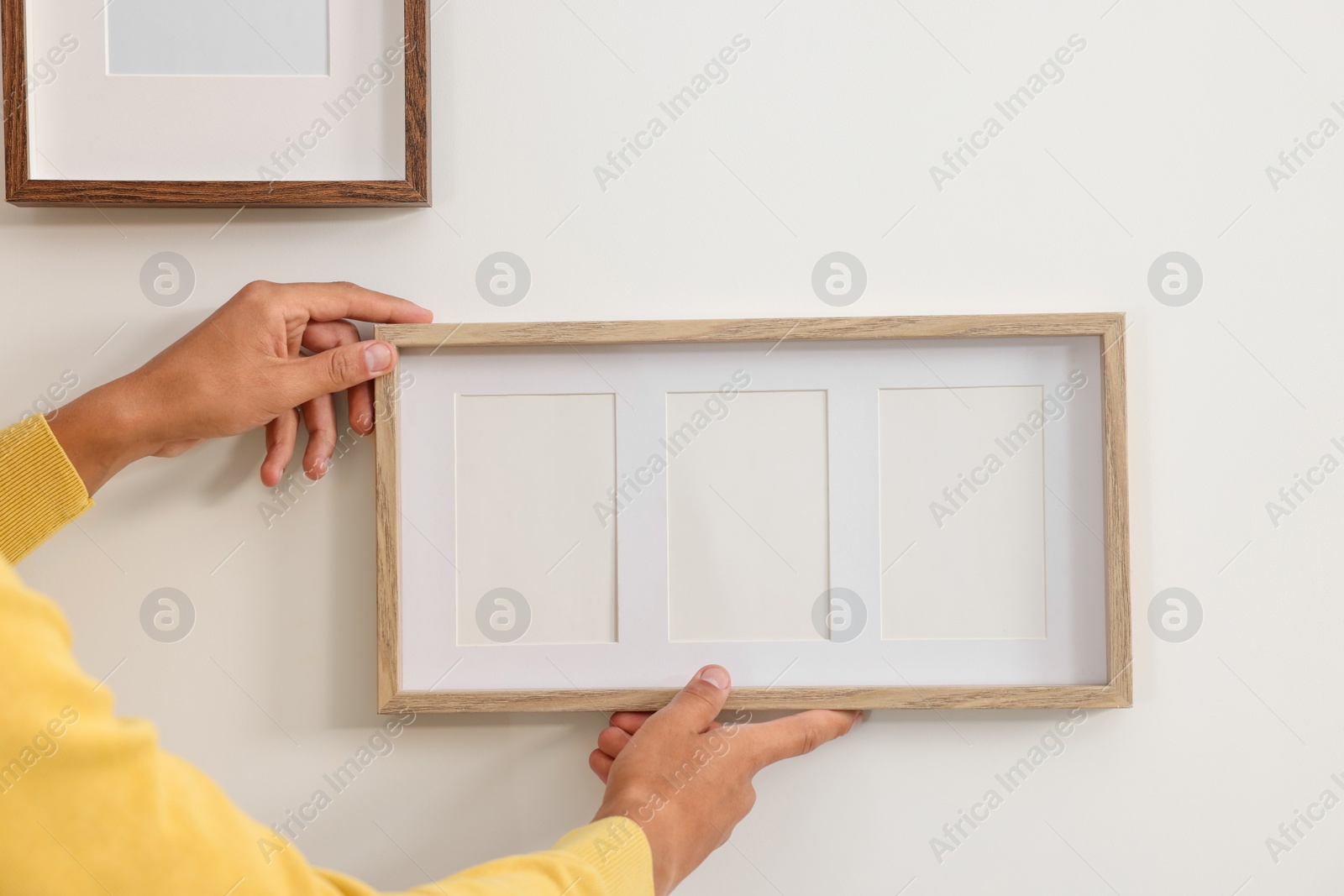 Photo of Young man hanging picture frames on white wall indoors, closeup. Space for text