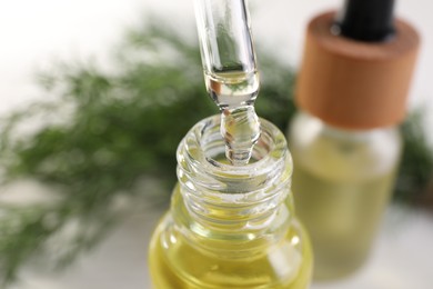 Photo of Dripping dill essential oil from pipette into bottle on blurred background, closeup