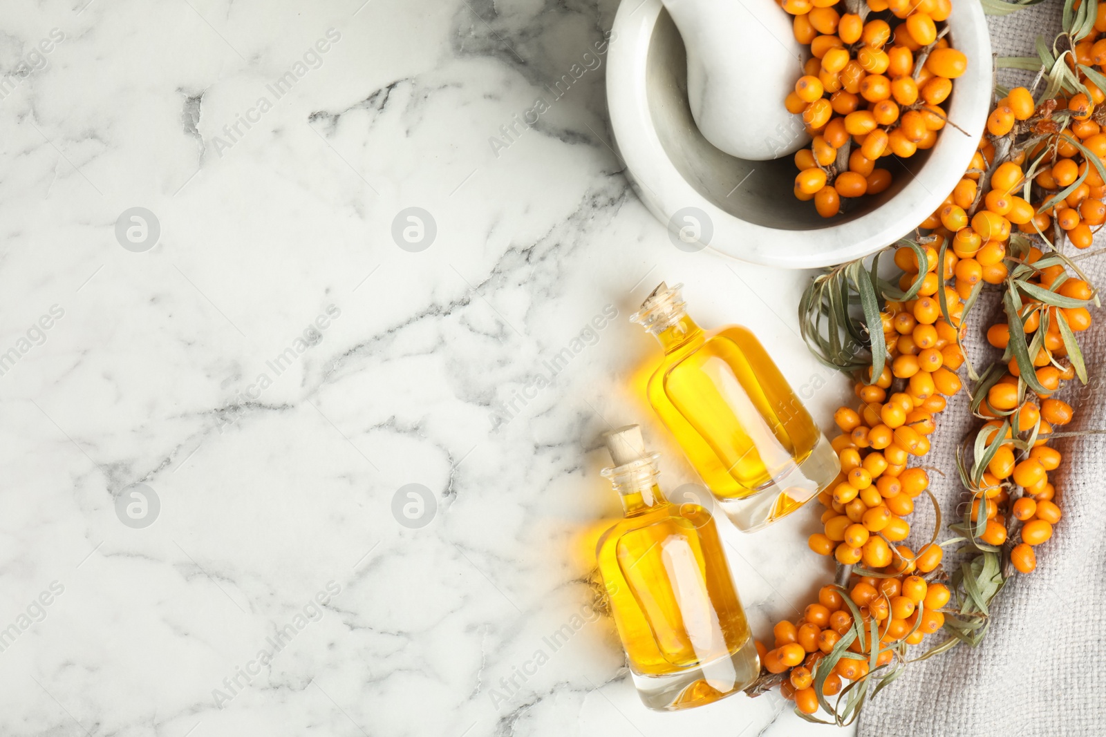 Photo of Natural sea buckthorn oil and fresh berries on white marble table, flat lay. Space for text