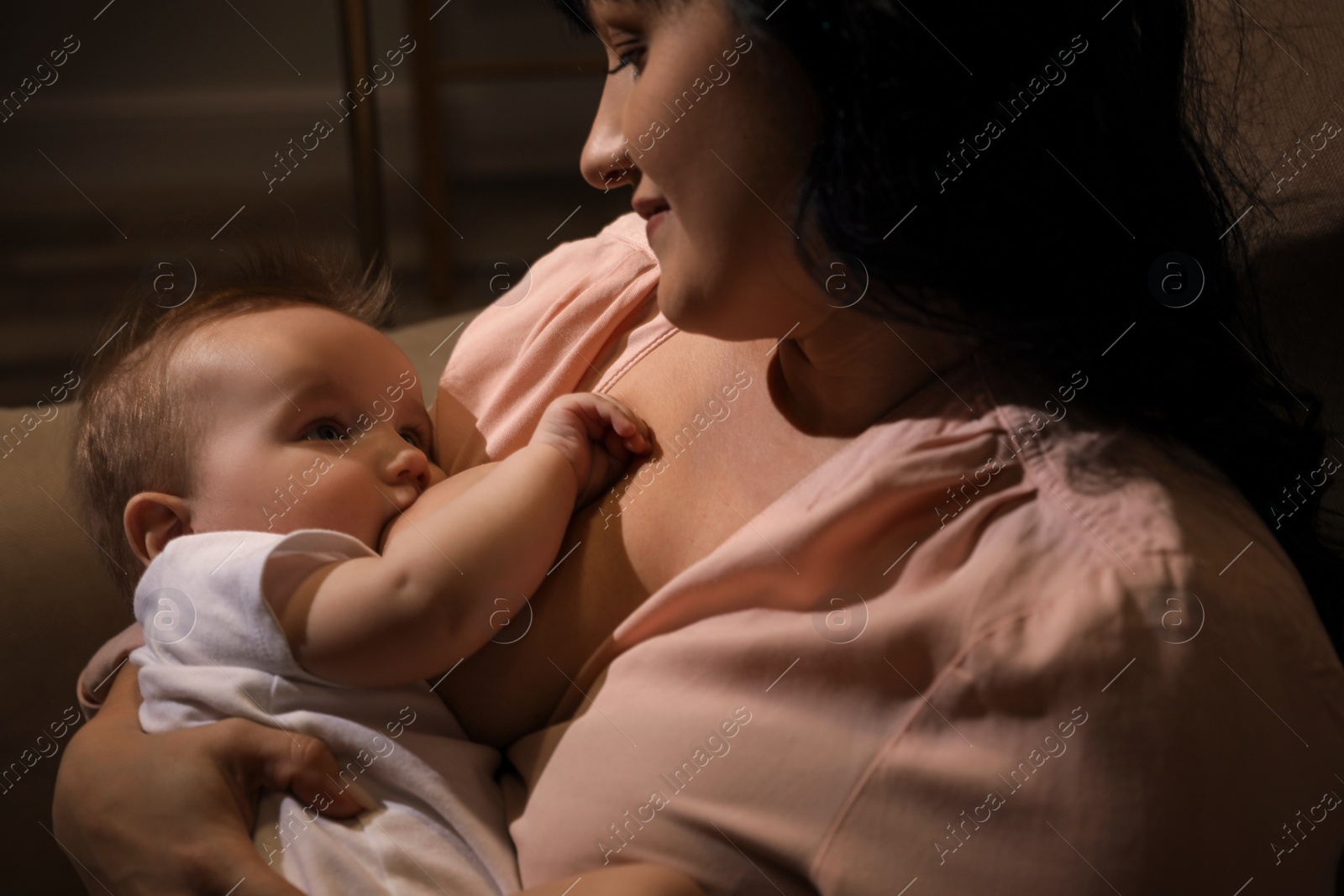 Photo of Woman breastfeeding her little baby on sofa in evening